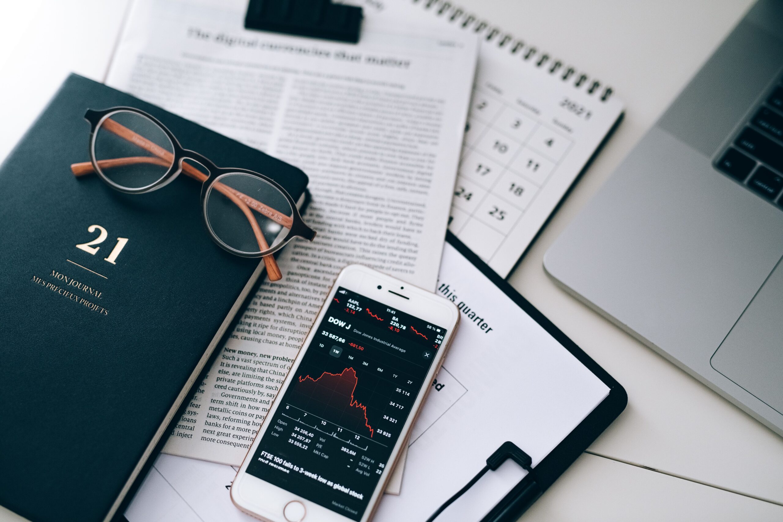 MBA in Finance: Career Opportunities, Benefits & Long-Term Growth Guide A stylish workspace featuring financial documents, eyeglasses, an iPhone displaying stock data, and a laptop.
